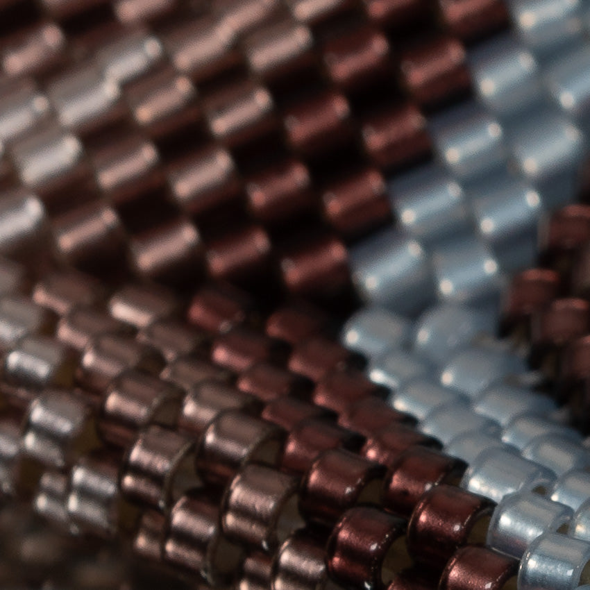 Close-up of hand-woven silver-lined plum ombre and light sapphire cylinder beads in a diagonal pattern