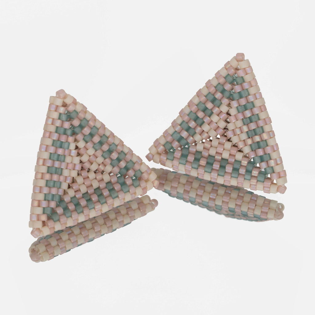 Pair of hand-woven blush, cream, and seafoam beaded triangle earrings, standing on a mirror