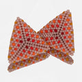 Pair of hand-woven blush, orange, and red beaded triangle earrings, standing on a mirror