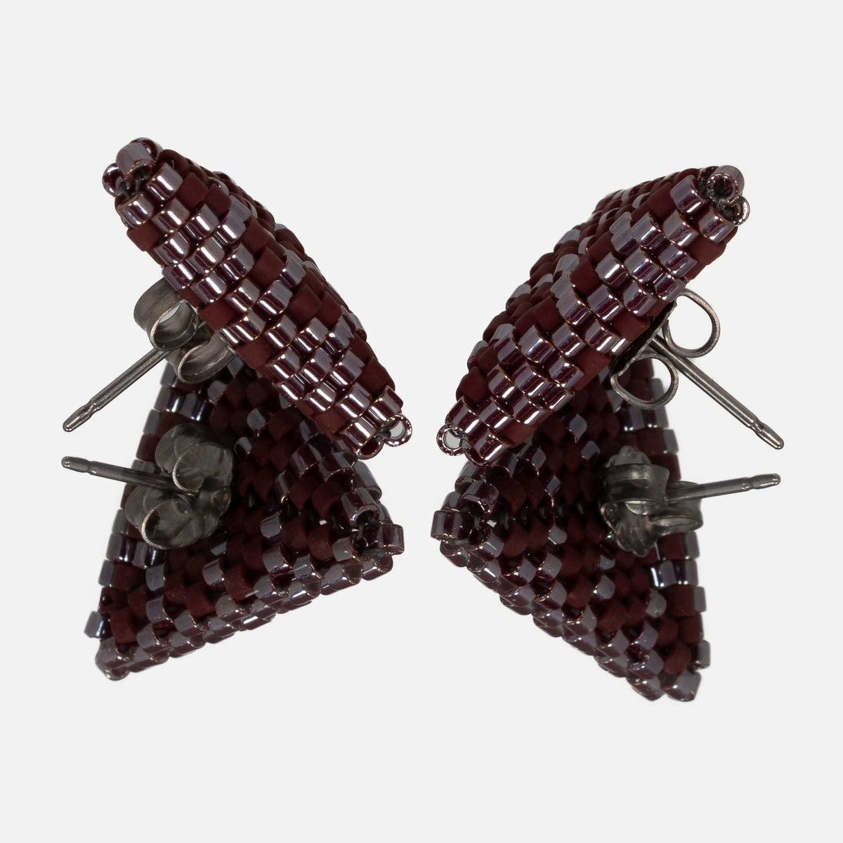 Pair of burgundy beaded triangle earrings facing each other on a mirror, showing the titanium posts and the woven edges