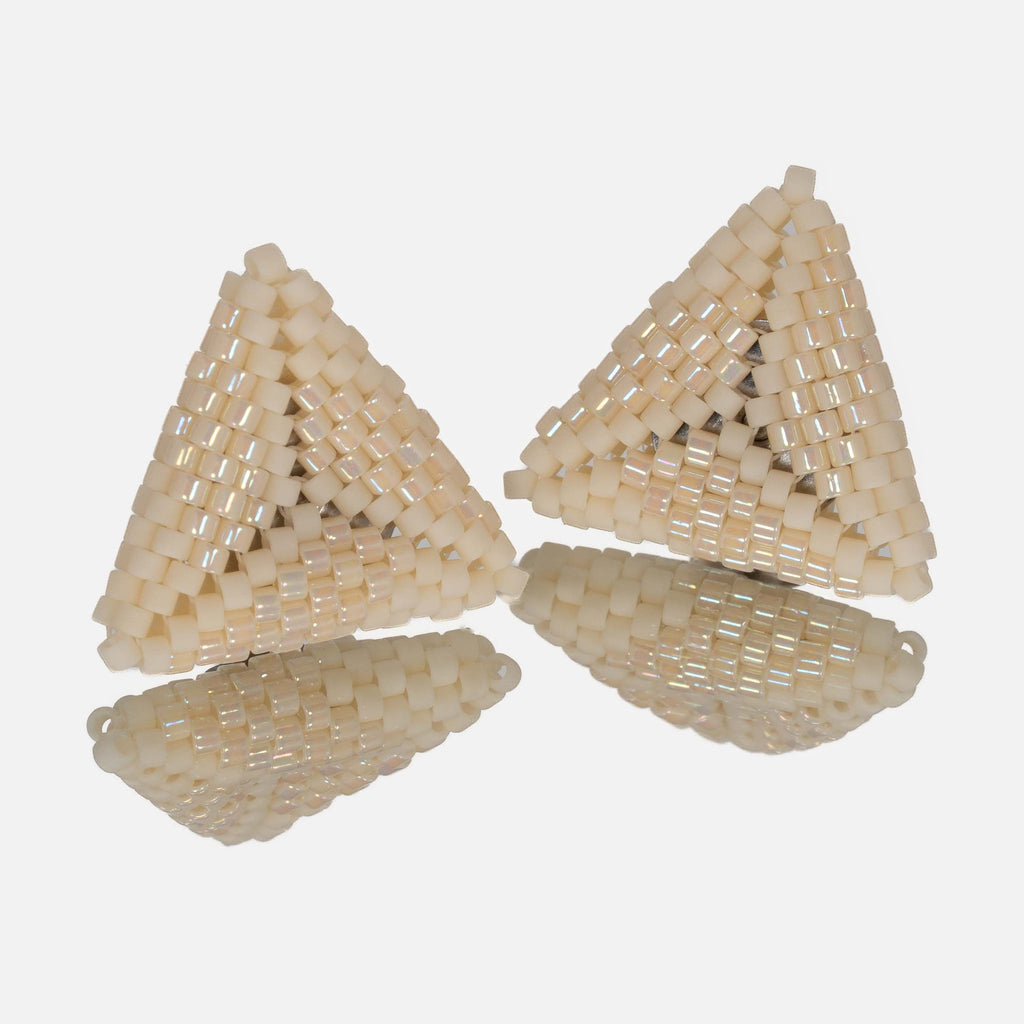 Pair of small hand-woven beaded triangle earrings in matte and iridescent cream, standing on a mirror
