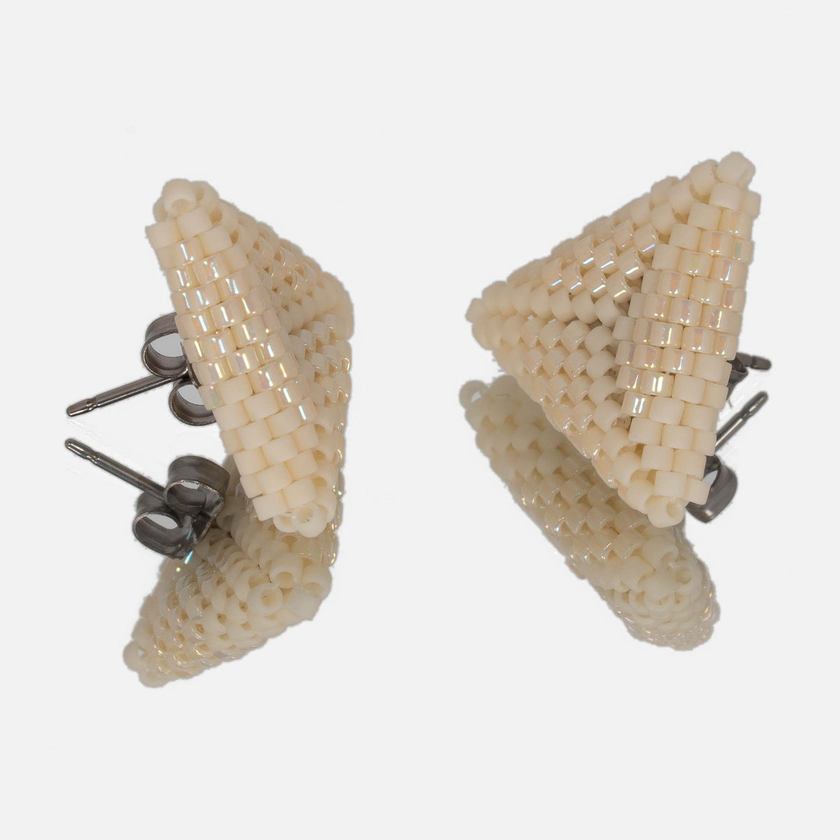 Pair of cream and iridescent beaded triangle earrings facing each other on a mirror, showing the titanium posts and the woven edges