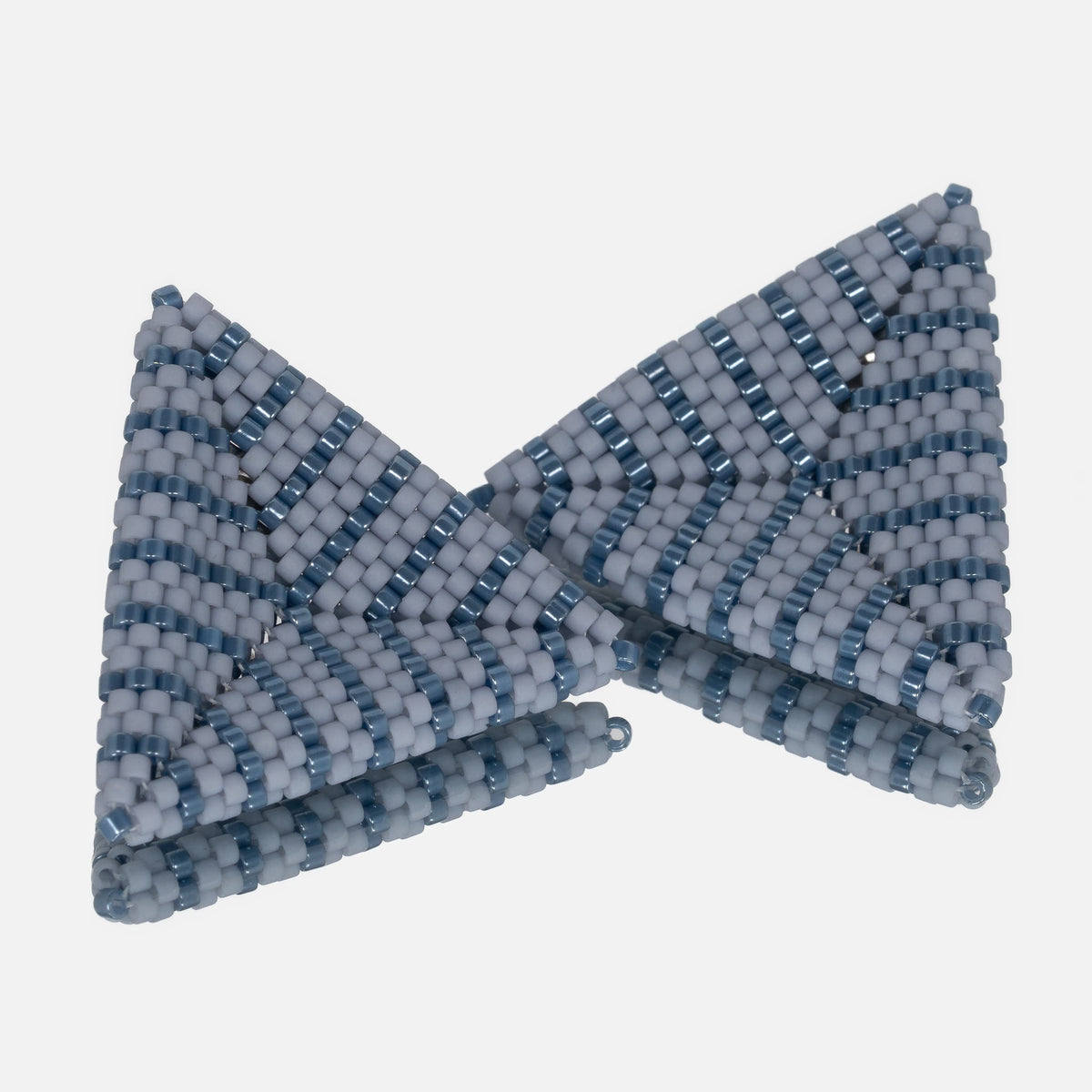 Pair of hand-woven beaded triangle earrings with matte dusty blue and luster denim stripes, standing on a mirror