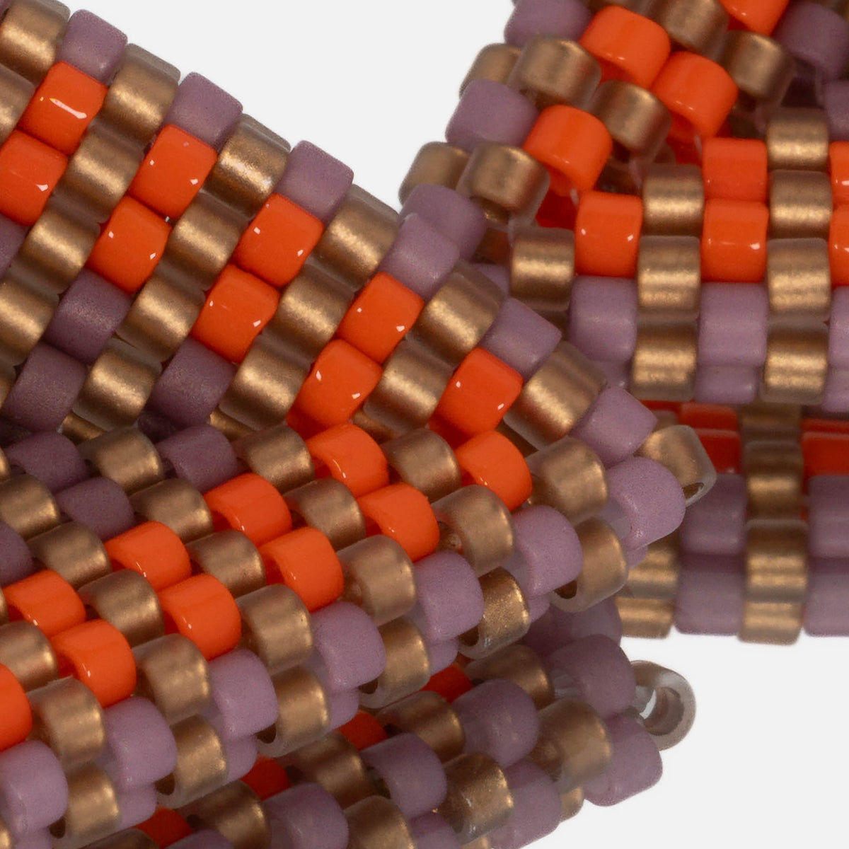 Close-up of matte lilac, matte gold, and glossy sunset orange cylinder beads woven in peyote stitch