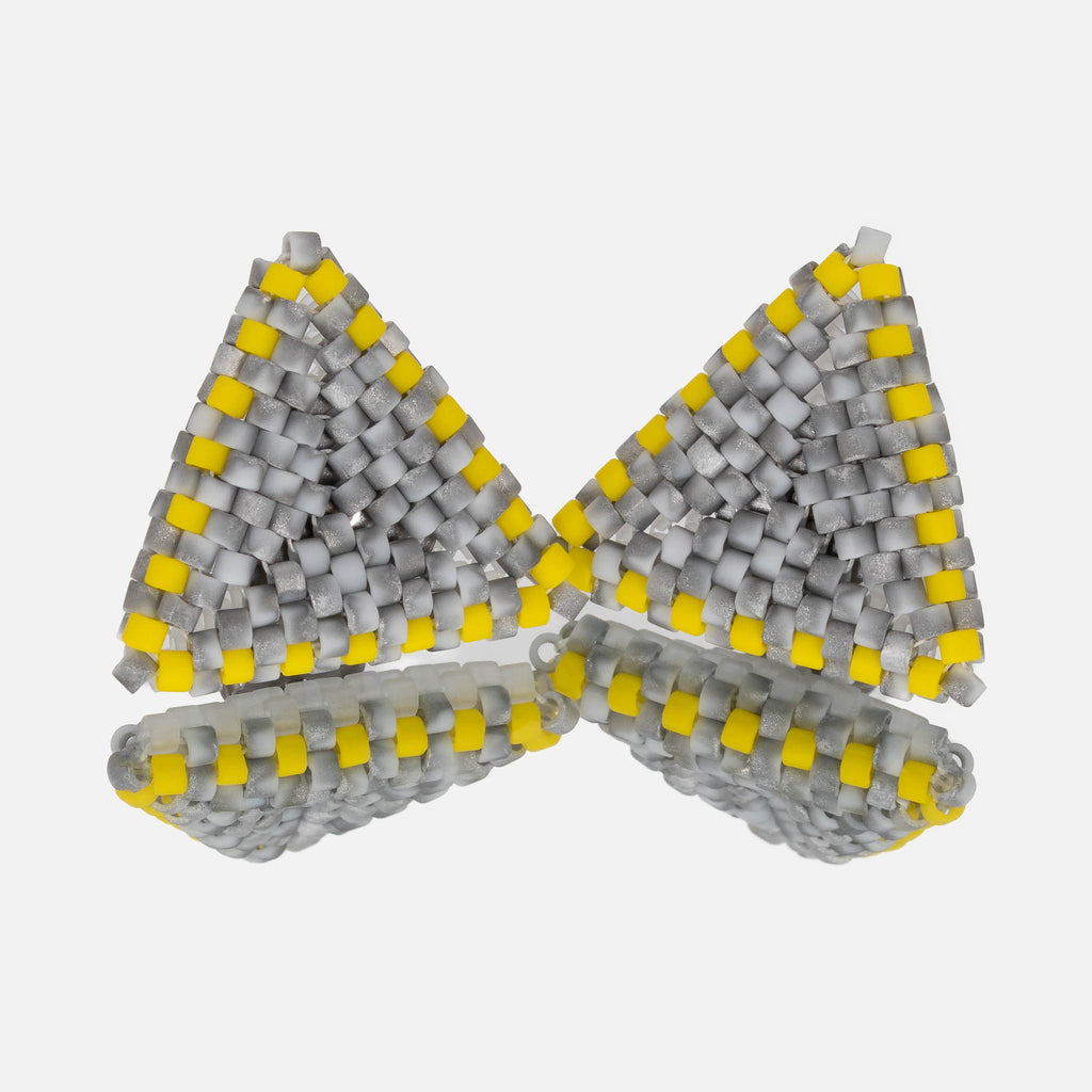 Pair of small hand-woven beaded triangle earrings in mottled gray with yellow edges, standing on a mirror