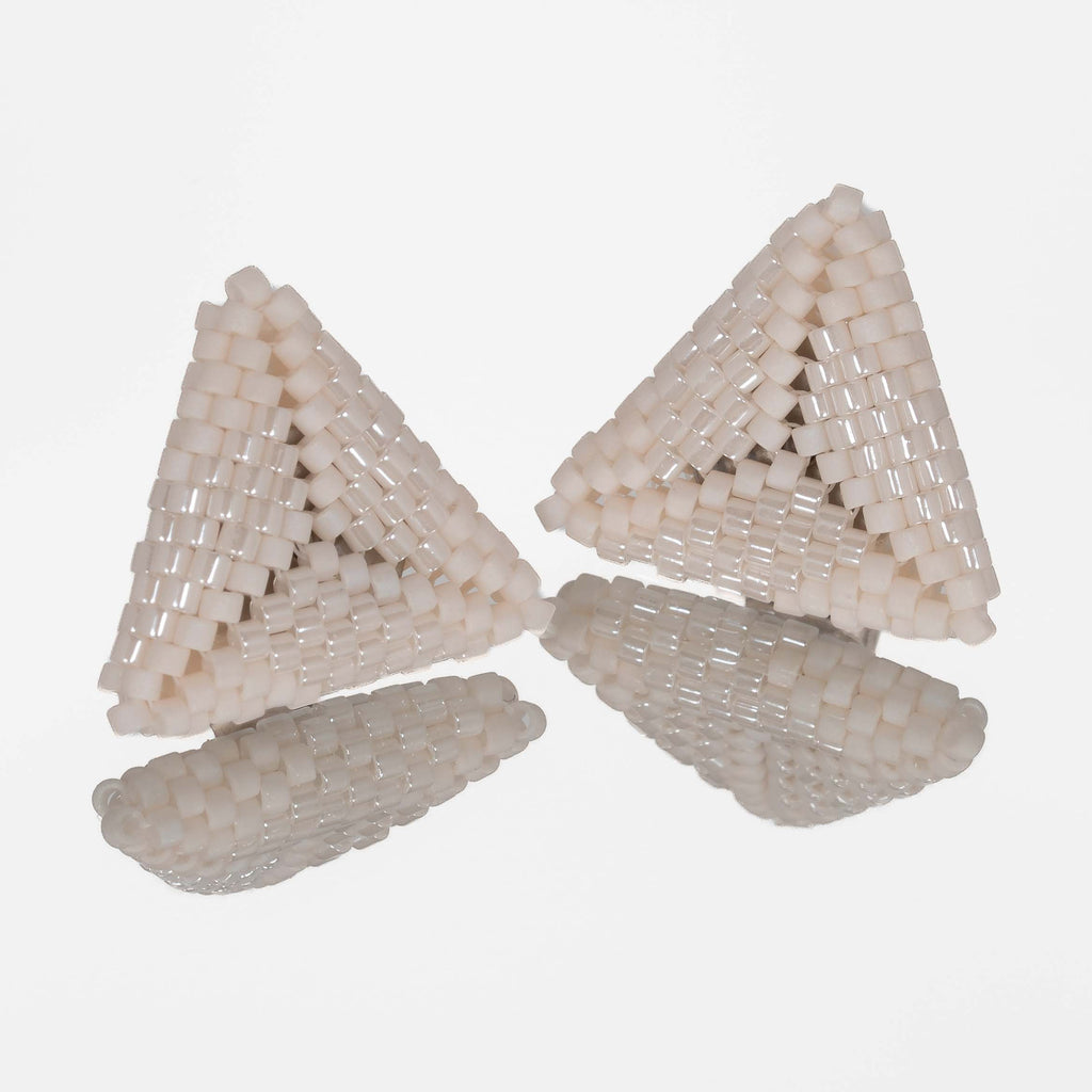 Pair of small hand-woven beaded triangle earrings in matte and pearly ivory, standing on a mirror