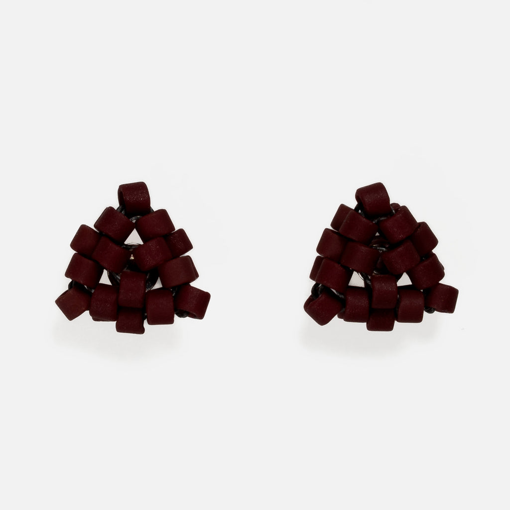 Pair of tiny triangular beaded stud earrings in matte deep burgundy red, front view on a light gray background