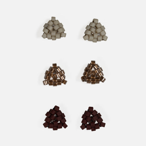 Three pairs of tiny triangular beaded stud earrings in matte greige, antique copper-lined glass, and matte oxblood, arranged in rows on a light gray background
