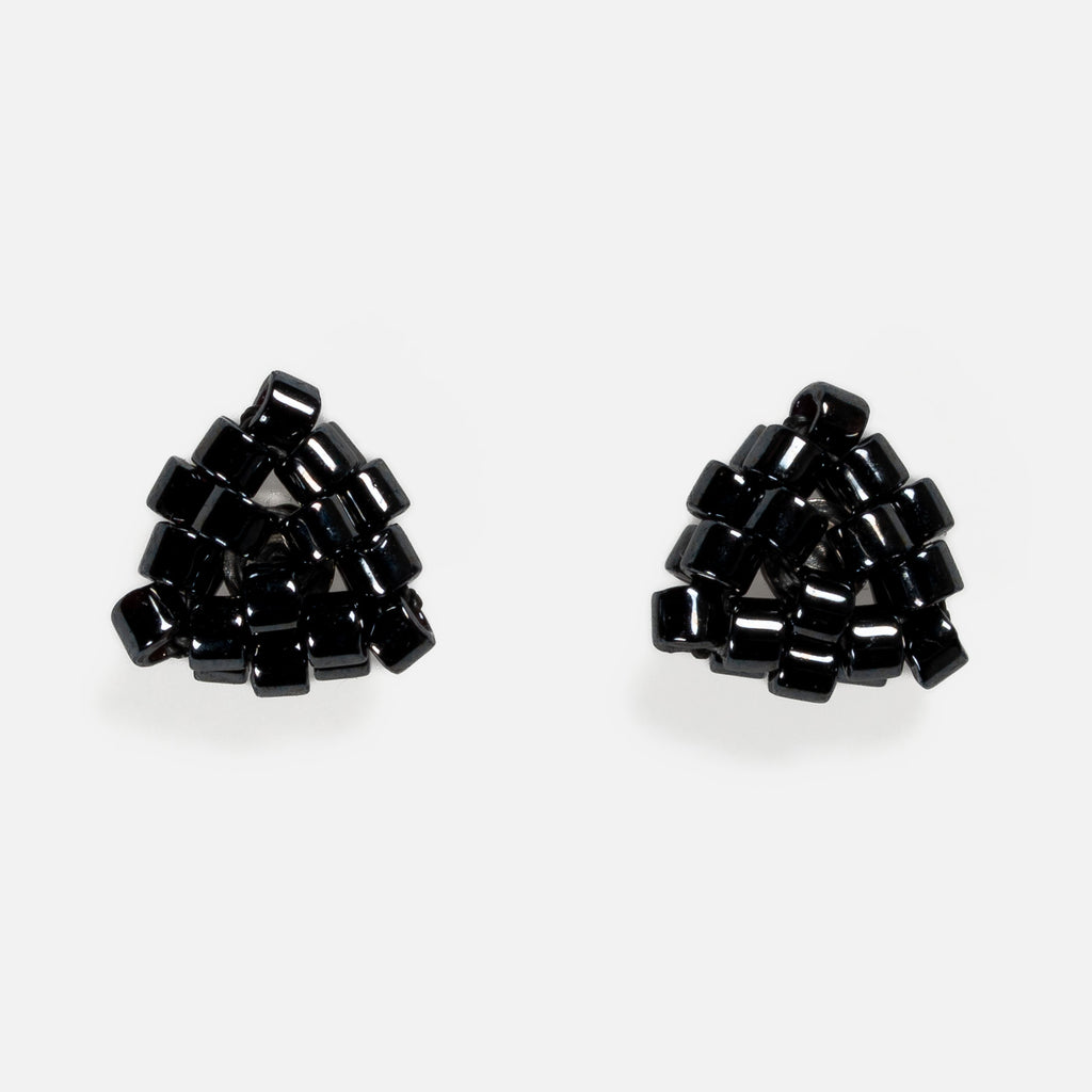Pair of tiny triangular beaded stud earrings in near-black gunmetal metallic beads, front view on a light gray background