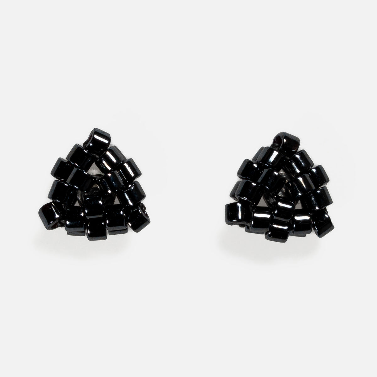 Pair of tiny triangular beaded stud earrings in near-black gunmetal metallic beads, front view on a light gray background