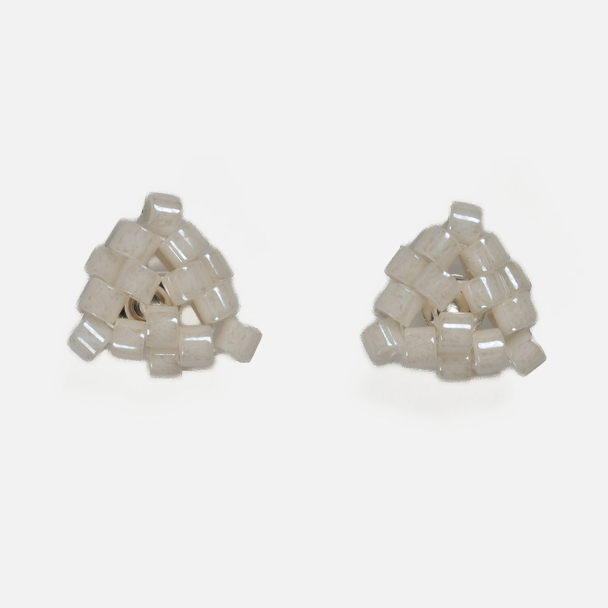 Pair of tiny triangular beaded stud earrings in warm ivory with a pearly luster, front view on a light gray background