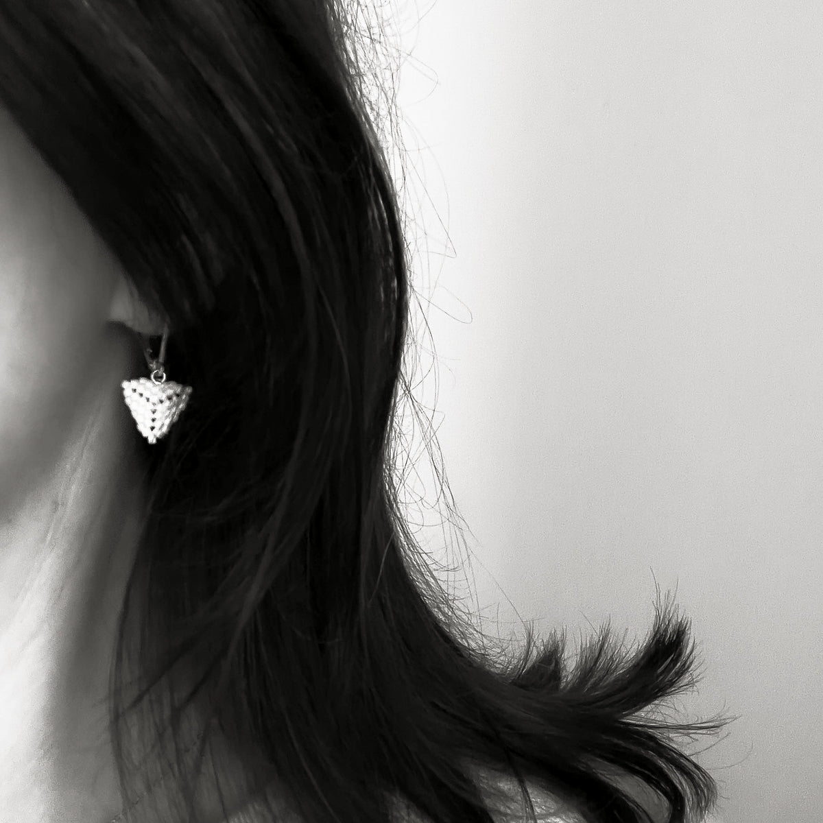 Black and white photo of an interchangeable lever-back earring with a beaded triangle module, worn on an earlobe, shown for size.