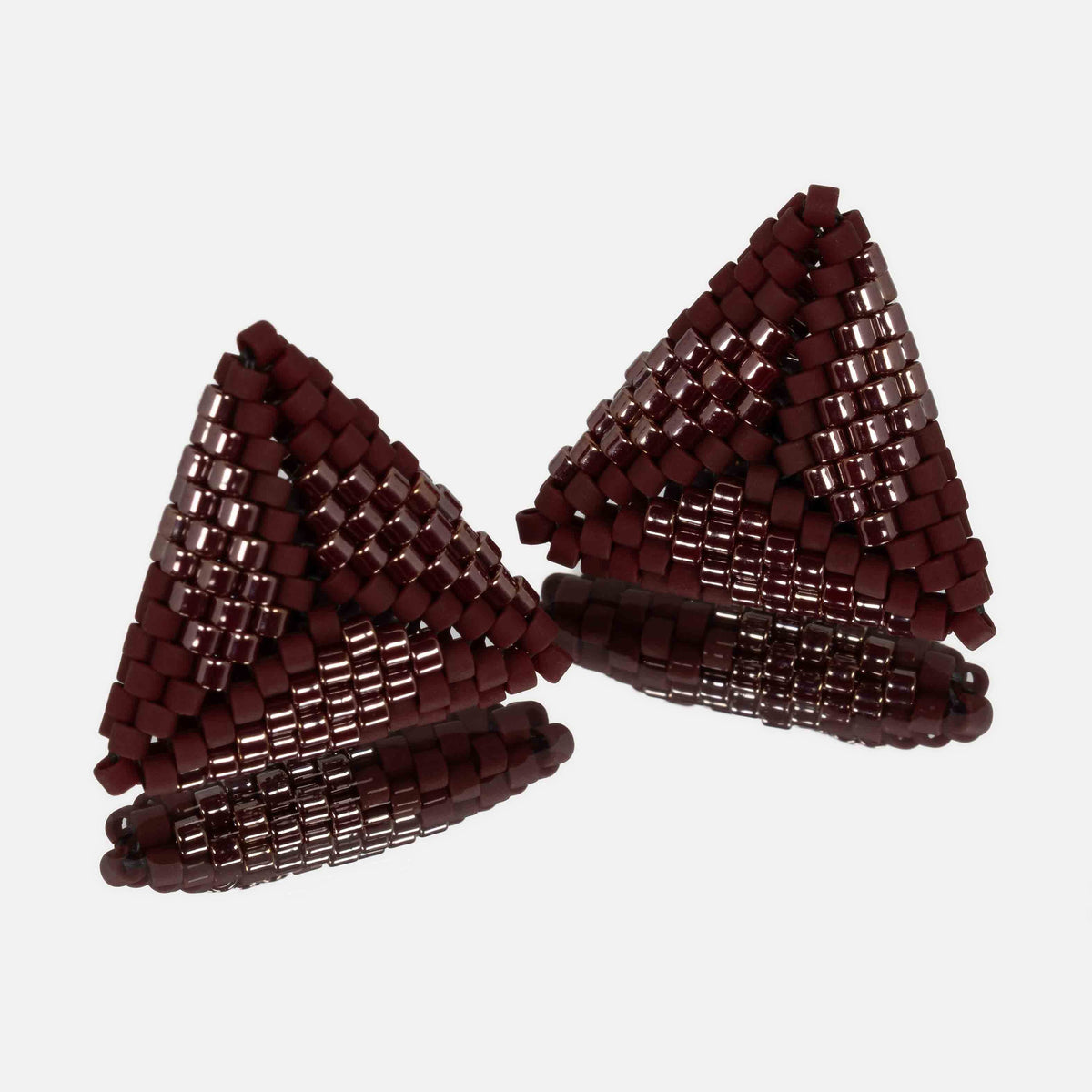 Pair of small hand-woven beaded triangle earrings in matte and luster burgundy, standing on a mirror