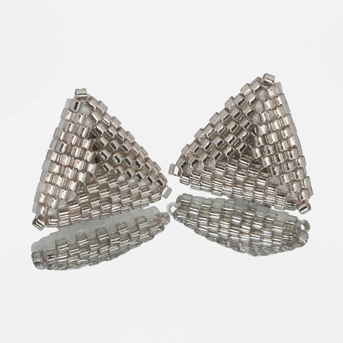Pair of hand-woven silver-lined beaded triangle earrings, standing on a mirror